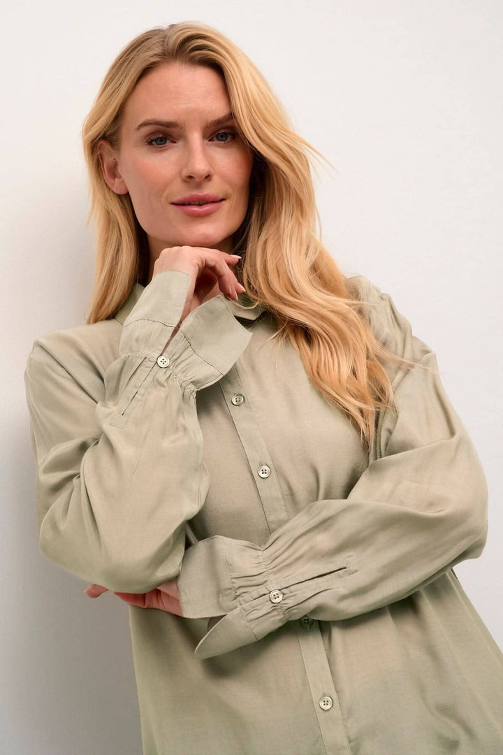 Femme souriante portant une chemise Arina en vert, avec manches longues et coupe décontractée, style intemporel.
