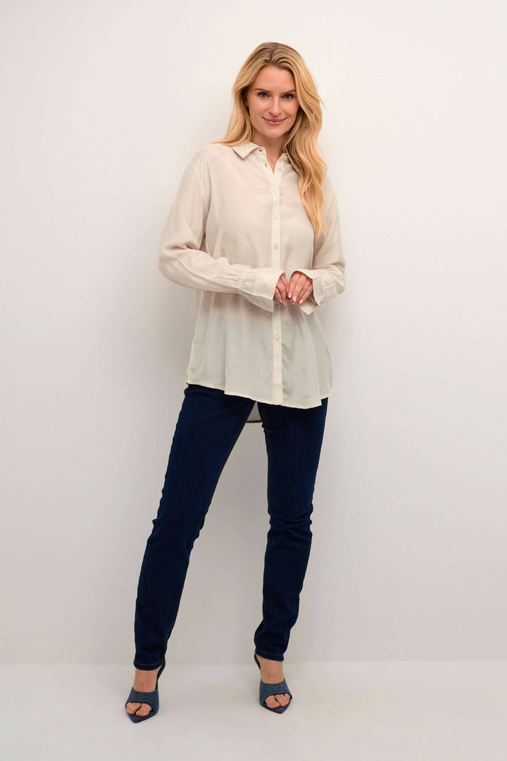 Femme portant une chemise Arina blanche à manches longues, jean bleu et chaussures à talons.