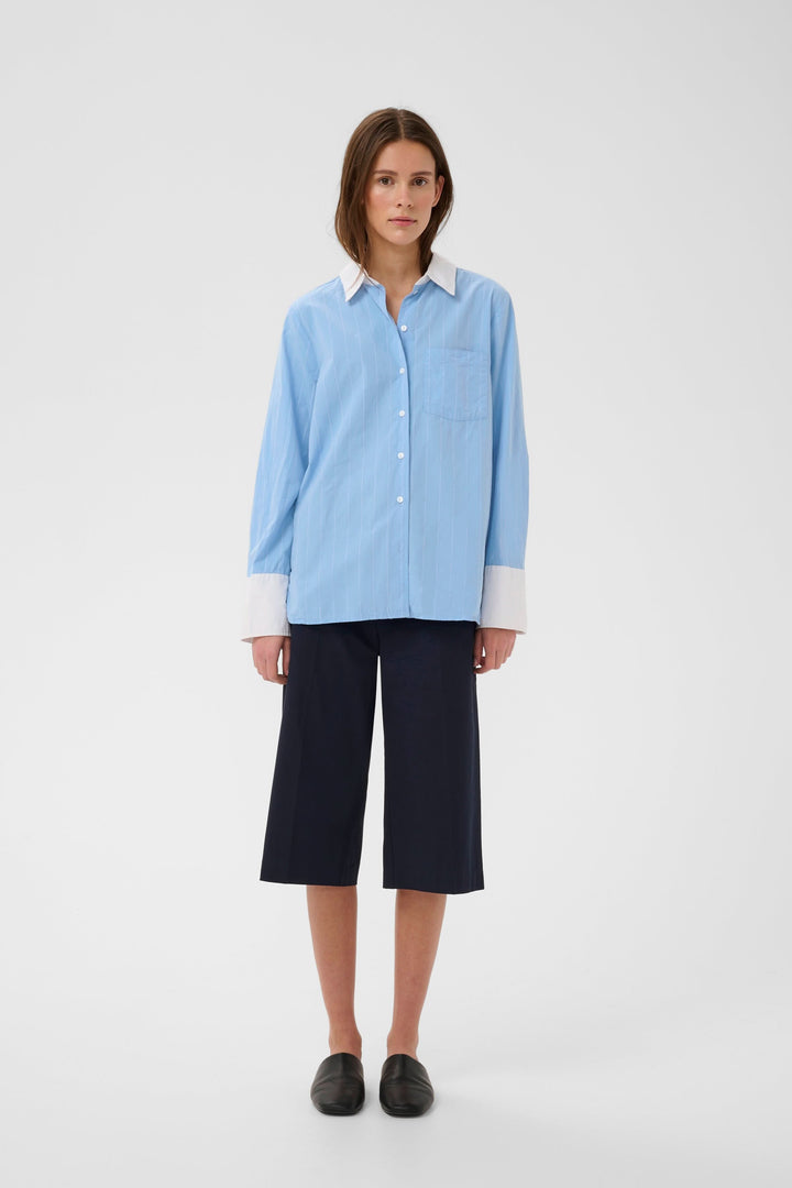 Chemise Dessy rayée à col contrastant en bleu avec manches longues, portée par une femme, style moderne et soigné.