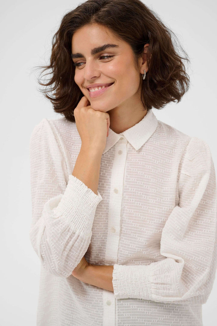 Femme portant la chemise Penelope texturée à manches bouffantes, élégante avec col chemise et poignets smockés, style moderne.