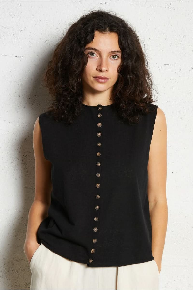 Femme portant une chemise sans manches noire avec boutonnière devant, style moderne et élégant.