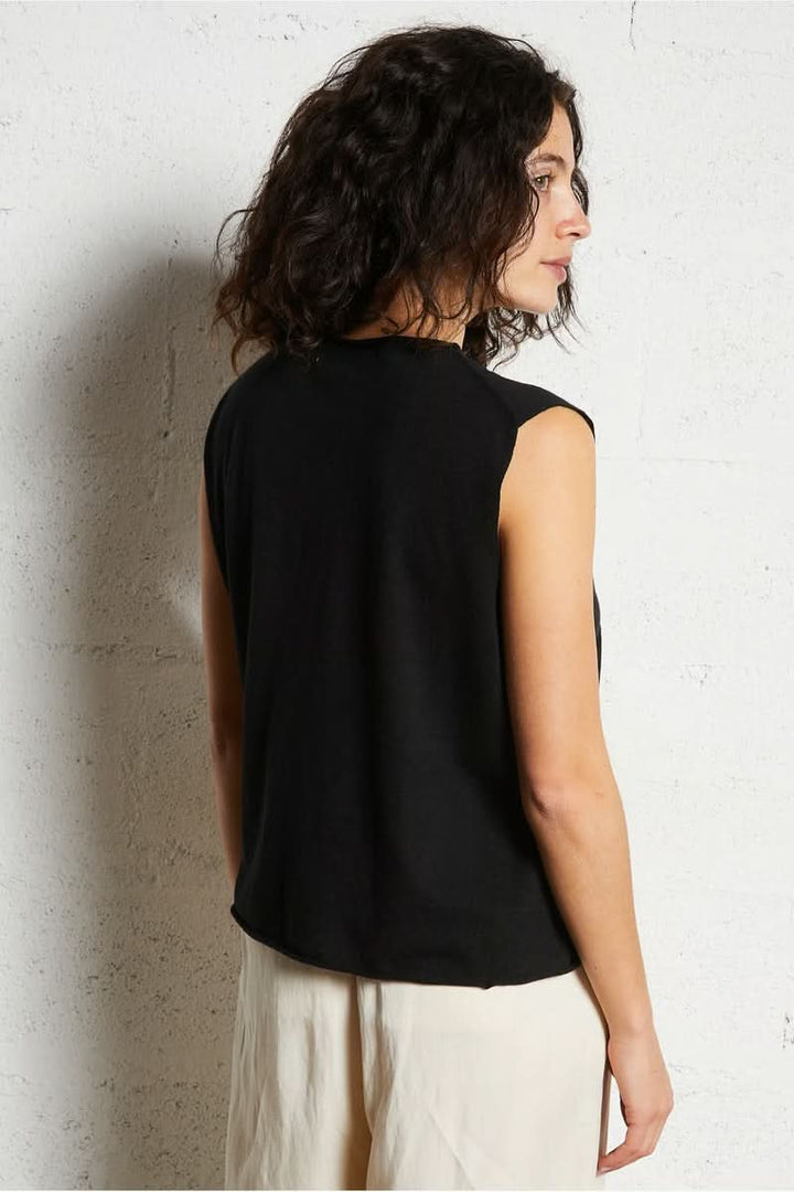 Femme portant une chemise sans manches noire, montrée de dos contre un mur blanc.