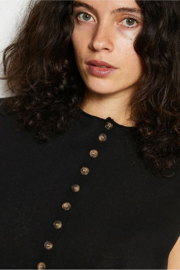 Femme portant un haut noir à boutons, regard intense