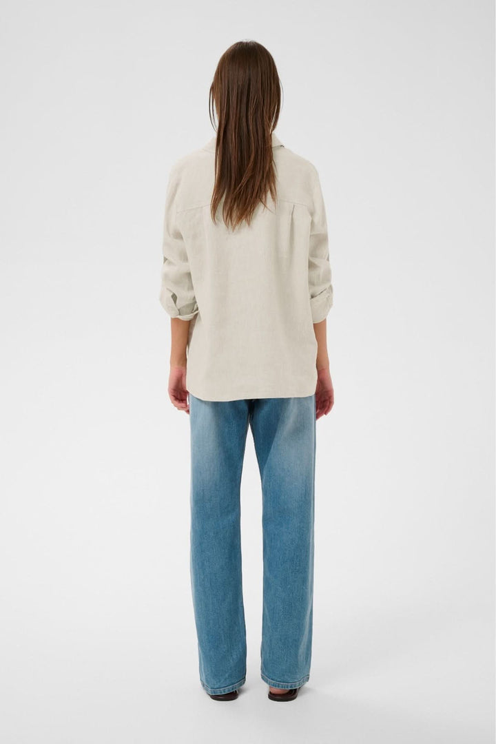 Femme portant une chemise en lin Dilana beige, vue de dos, avec manches retroussées et coupe fluide.