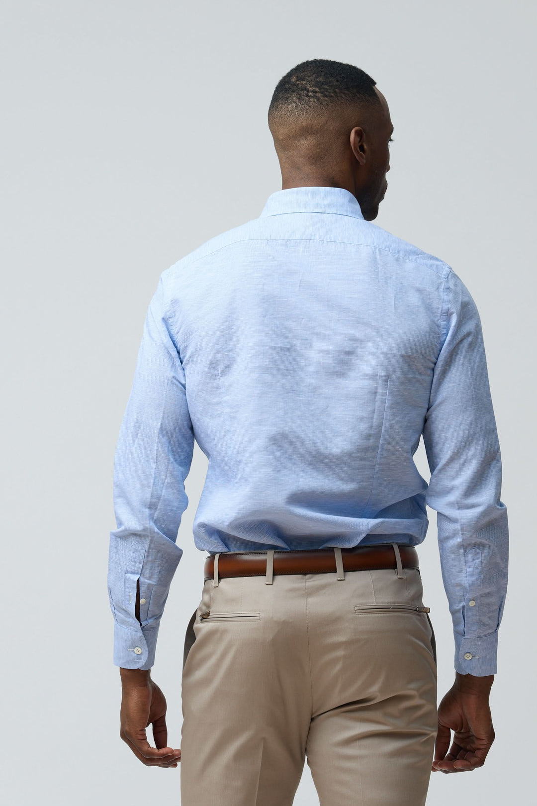 Homme portant une chemise en lin légère et raffinée bleue avec coupe ajustée, vue de dos, manches longues, col structuré classique.