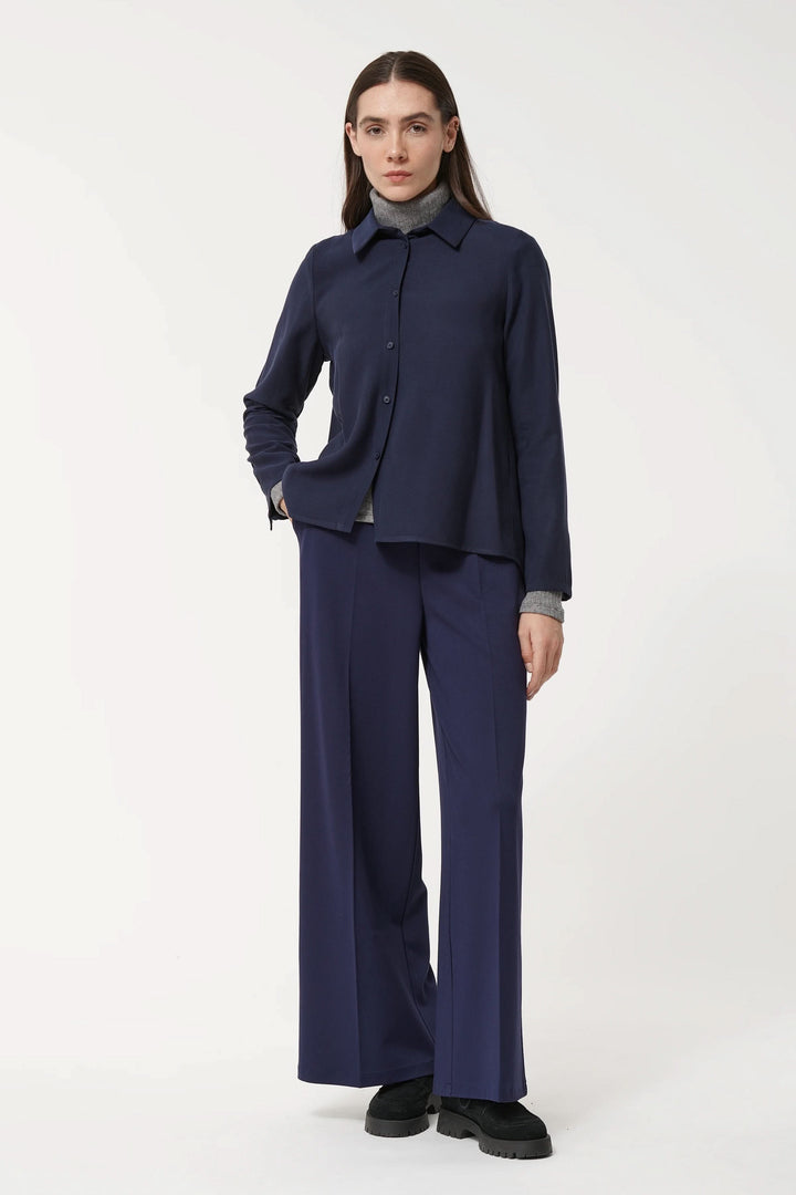 Chemise fluide bleu marine avec col classique, portée avec pantalon large pour un look élégant et confortable.