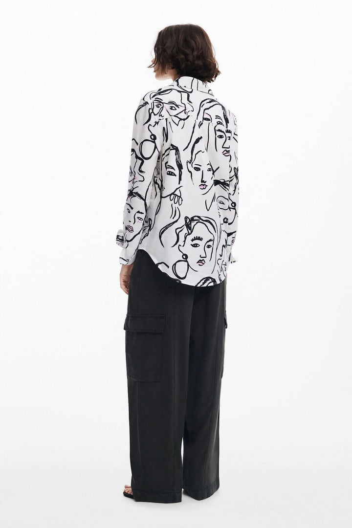 Chemise à manches longues avec imprimé de visages féminins, portée avec un pantalon noir, style chic.