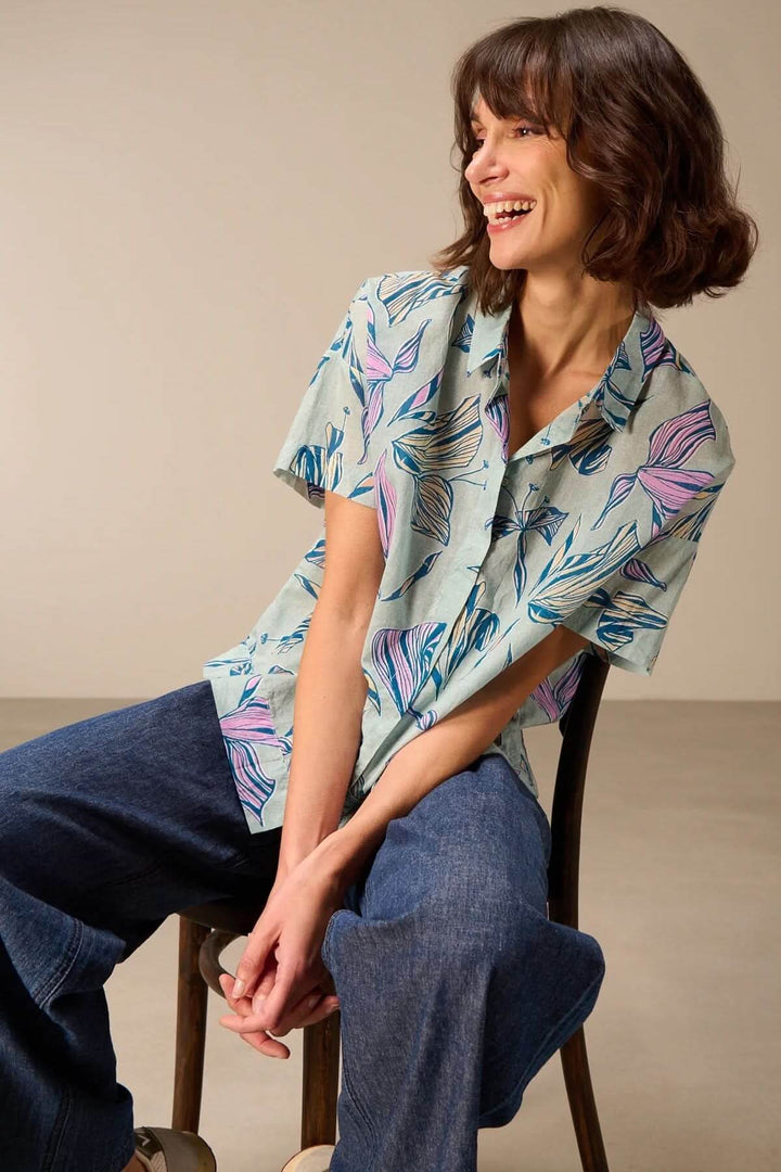 Femme portant une chemise légère à manches courtes avec imprimé floral, assise et souriante, tenue idéale pour l&