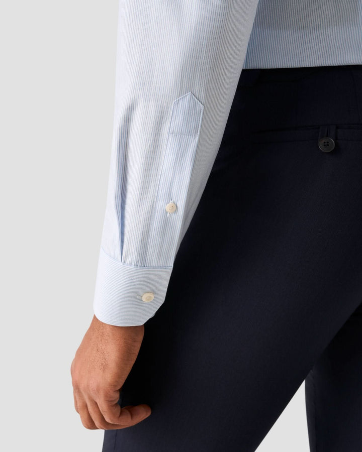Détail de la chemise lignée bleue claire avec col blanc et manche ajustée.