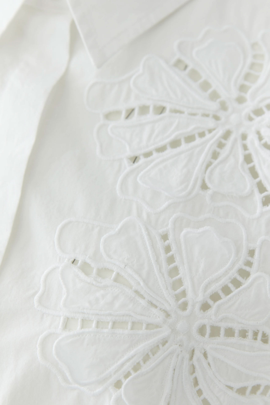 Chemise à manches courtes avec broderie délicate, vue en gros plan du détail brodé sur fond blanc.