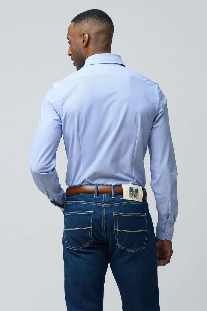 Homme portant une chemise structurée à micro-motif bleue, vue de dos, avec jeans et ceinture marron.