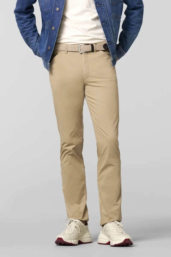 Pantalon chino ajusté beige porté avec un t-shirt blanc et une veste en jean, allié à des baskets blanches.