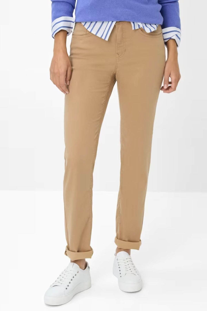 Chino de style Mary en camel, coupe ajustée, avec chaussures blanches, chemise rayée et pull bleu pour un look décontracté.
