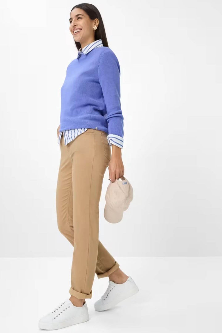Chino de style Mary en teinte camel, porté avec un pull bleu et une chemise rayée, pour un look casual chic élégant et contemporain.