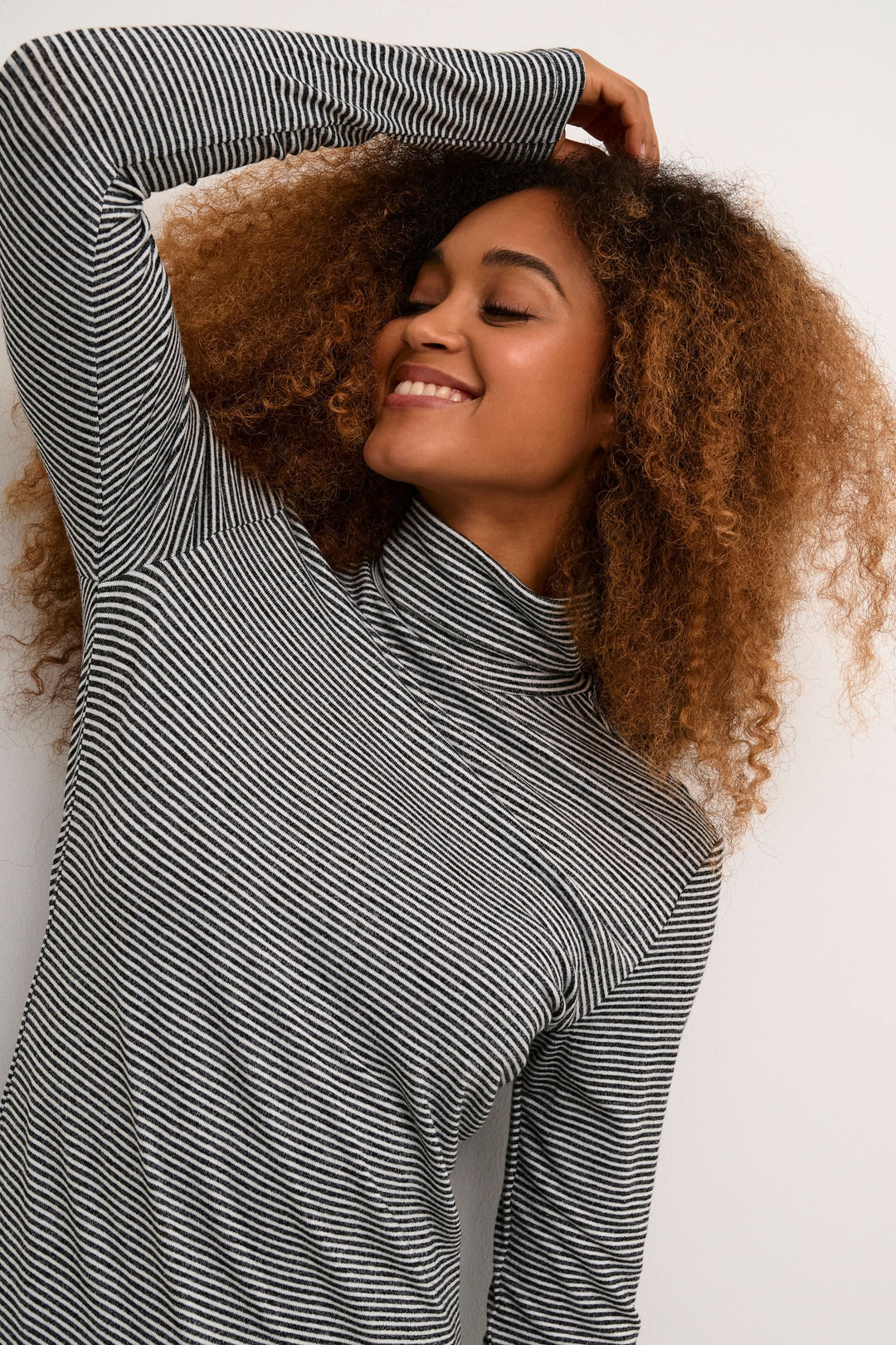 Femme souriante portant un col roulé rayé ajusté, parfait pour un look chic et moderne.