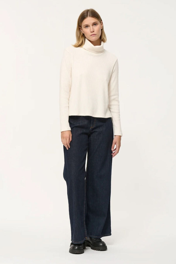 Femme portant un col roulé côtelé blanc avec un jean ample, parfait pour un look élégant et décontracté.
