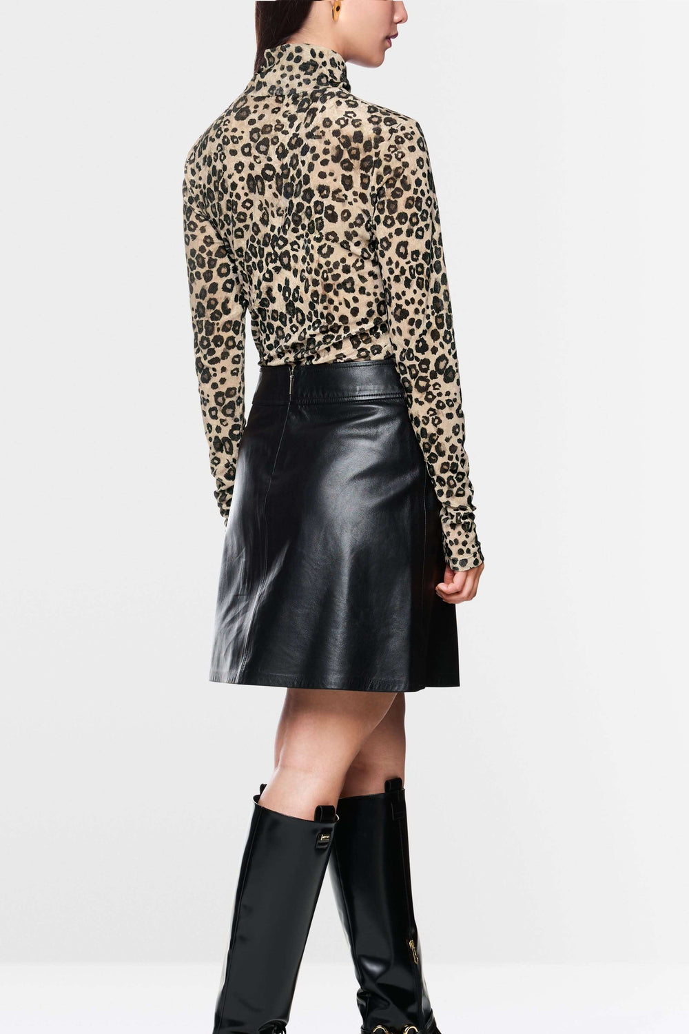 Femme vue de dos portant un col roulé léopard avec une jupe en cuir noire, pour un look chic et audacieux.