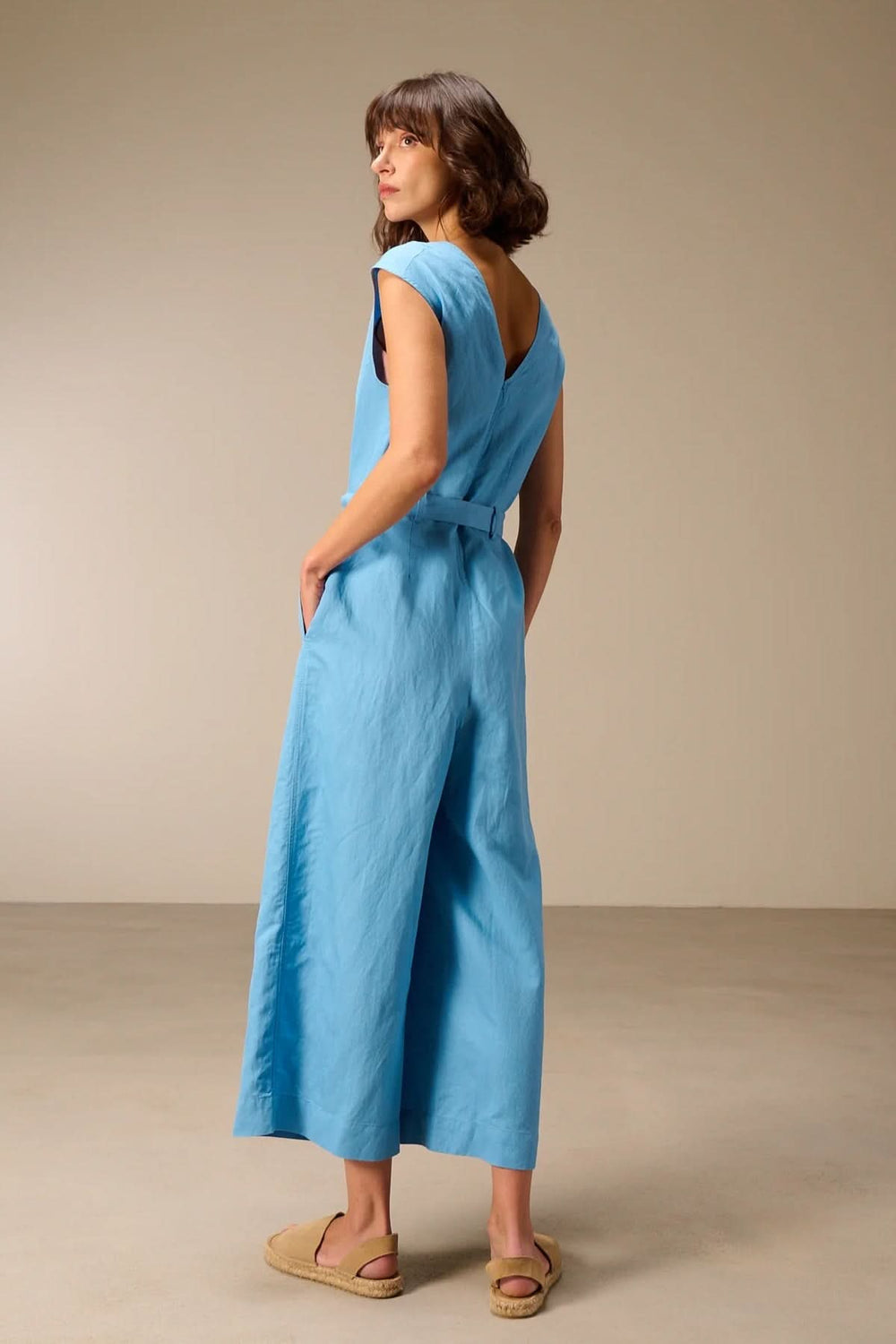 Femme portant une combinaison sans manches avec ceinture à nouer, tissu léger bleu, jambes larges.