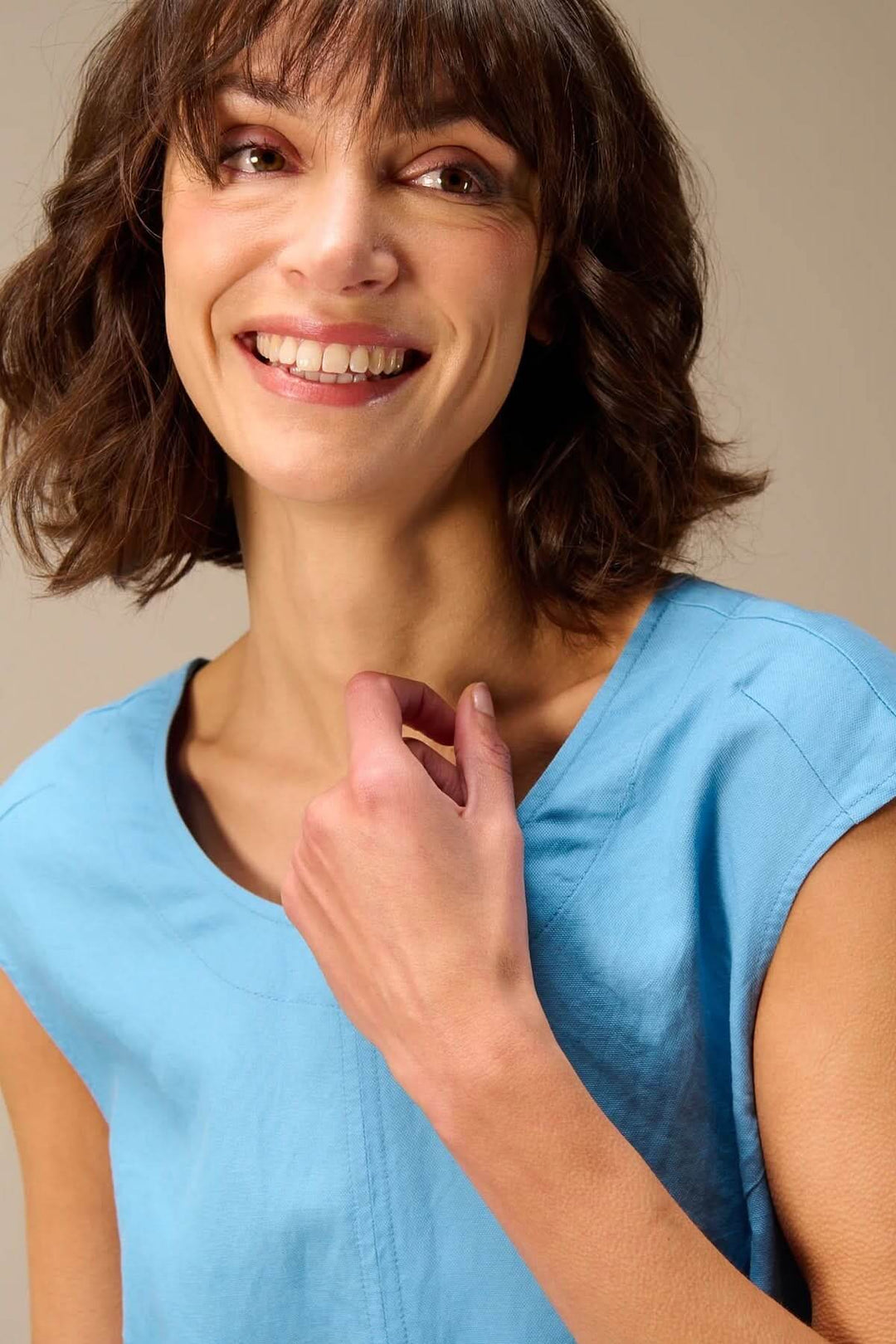 Femme souriante portant une tenue décontractée bleu clair à col rond, ambiance estivale et élégante.