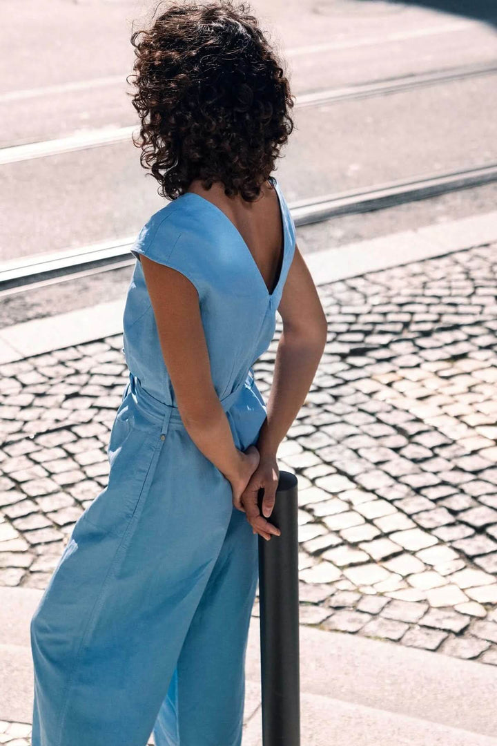 Femme portant une combinaison sans manches avec ceinture à nouer, style chic, en tissu léger pour un look estival moderne.