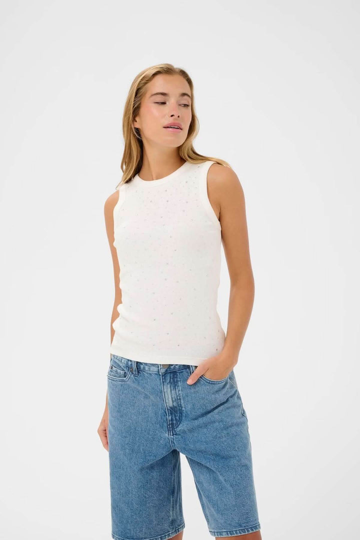 Débardeur sans manches en maille côtelée blanche avec détails de strass, porté avec un jean pour un look casual chic.