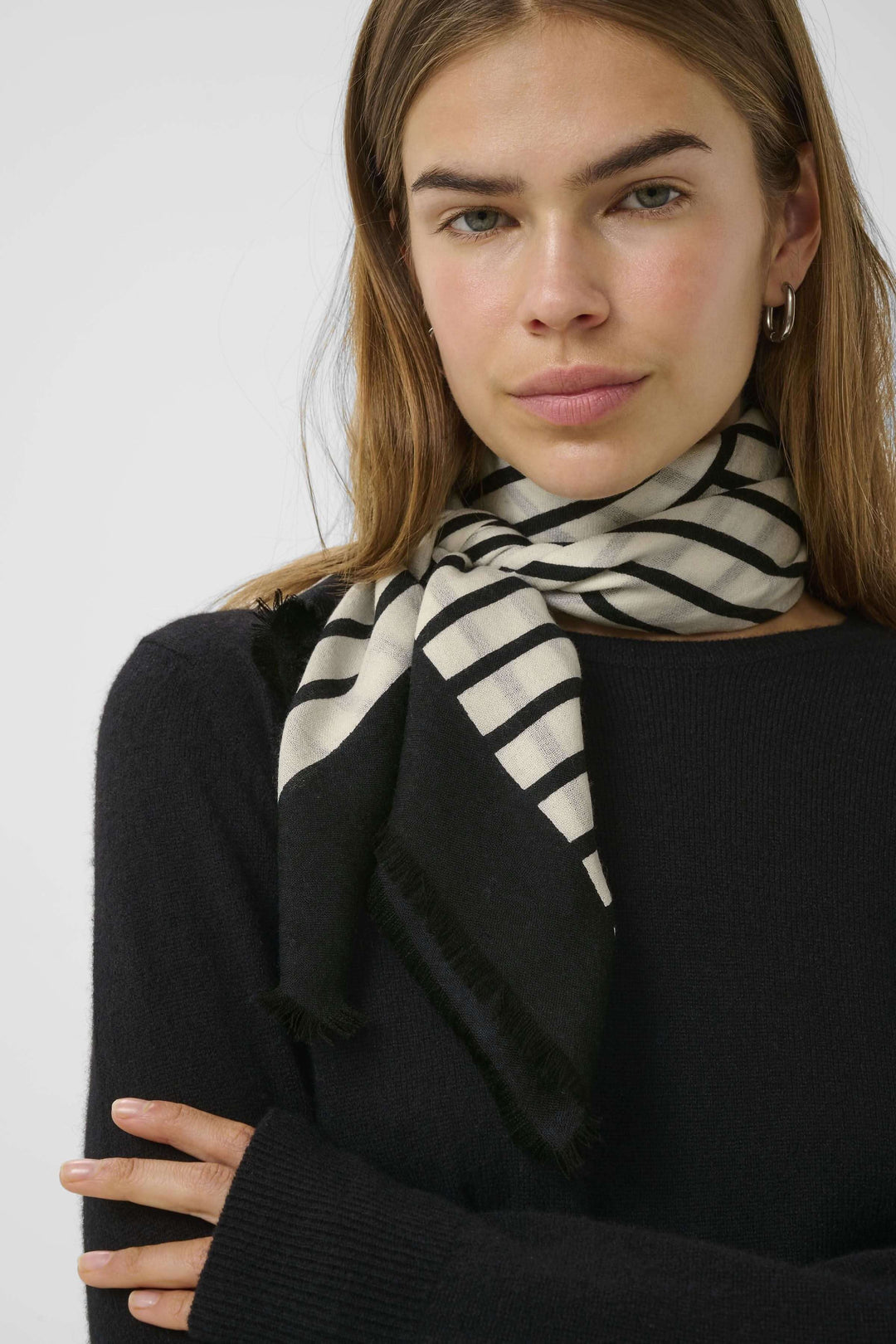 Foulard rayé moderne porté autour du cou, ajoutant une touche élégante à un pull noir.