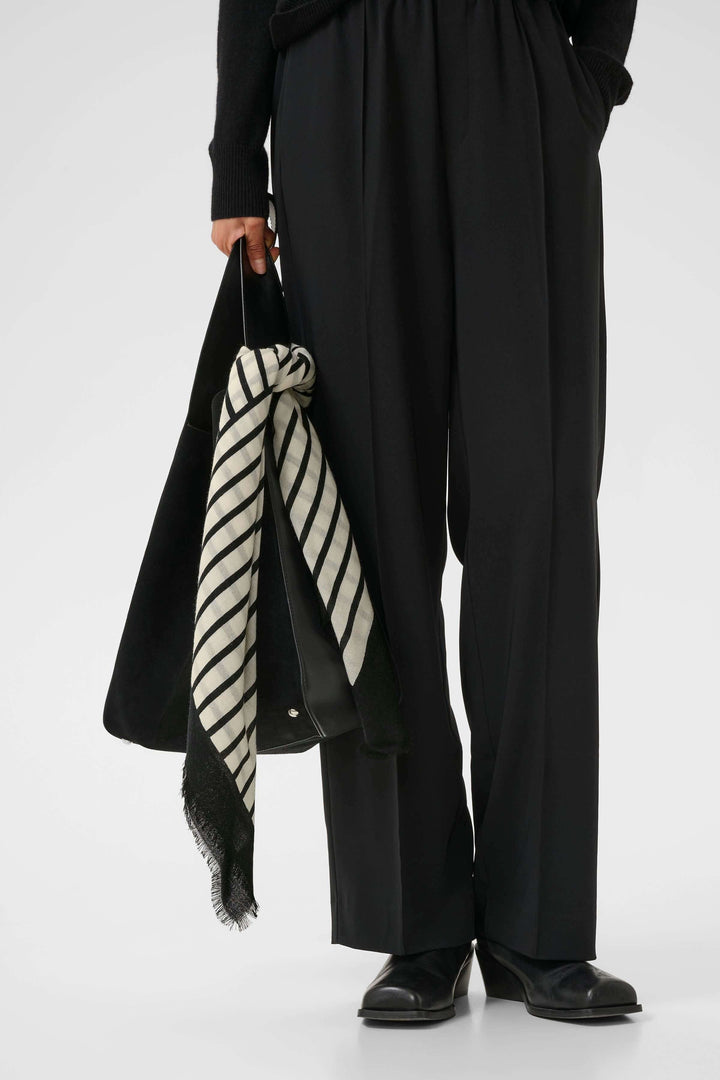 Foulard rayé moderne en noir et blanc, porté avec des pantalons noirs, ajoutant une touche élégante à la tenue.