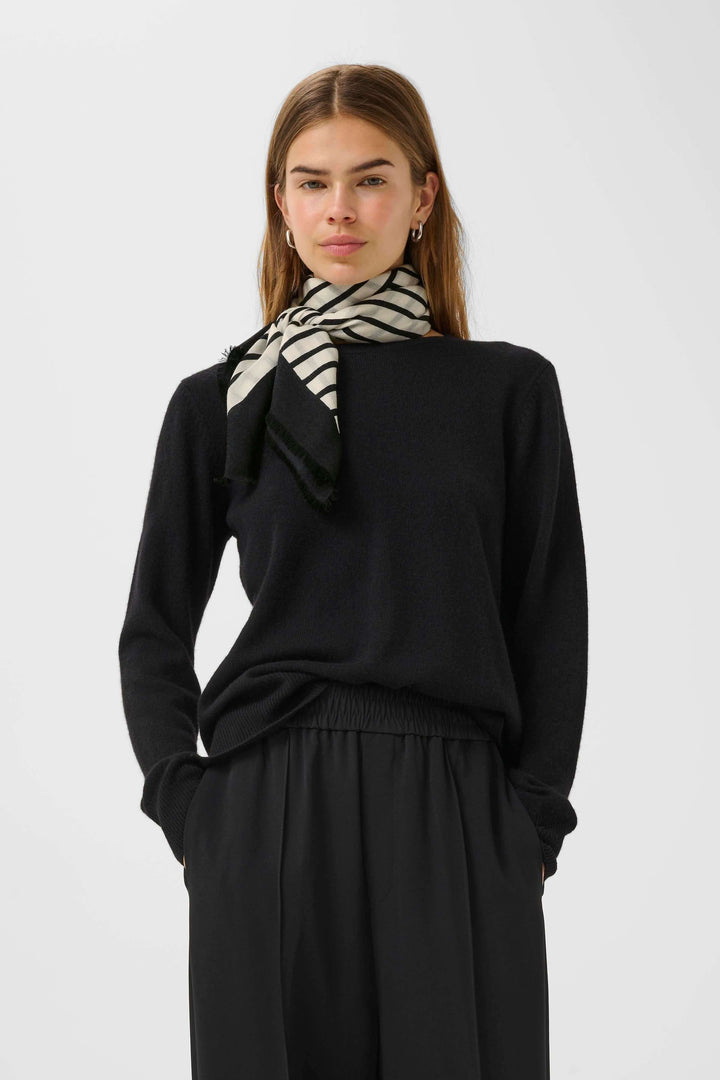 Modèle portant un foulard rayé noir et beige sur un chandail noir, ajoutant une touche élégante à son look.
