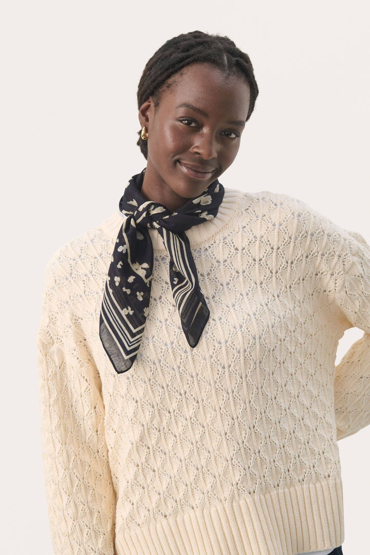 Foulard Phi élégant en coton, porté autour du cou avec un pull crème, ajoutant une touche de fraîcheur.