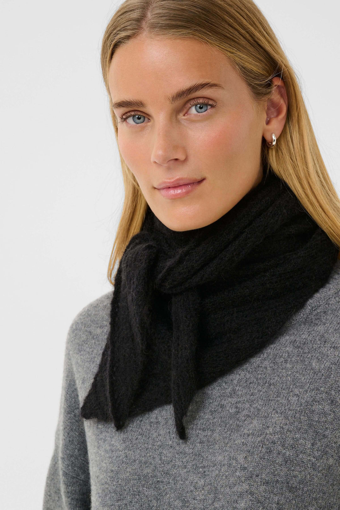 Femme portant un foulard tricoté noir au toucher duveteux, ajoutant une touche de raffinement discret à une tenue minimaliste.