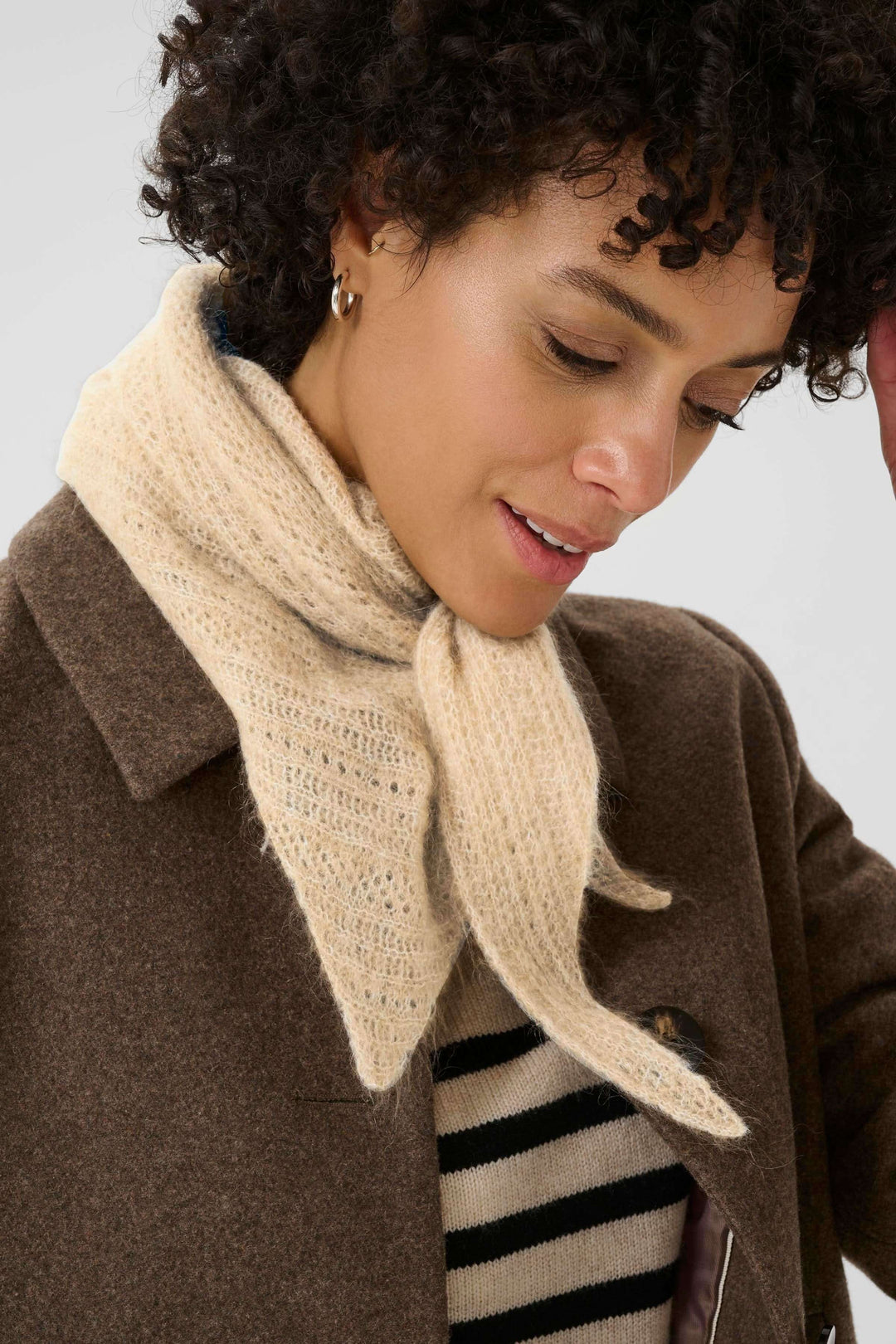 Foulard Sizze en tricot léger porté sous un manteau marron, offrant chaleur et style minimaliste moderne.