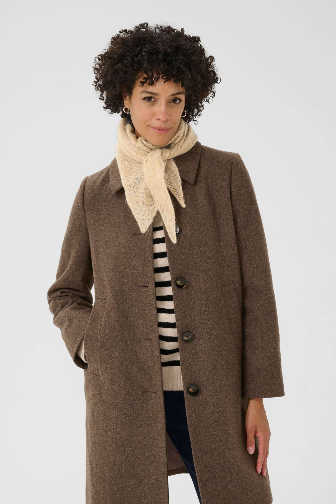 Femme portant un foulard Sizze en tricot léger sous un manteau marron ouvert, offrant un look minimaliste et moderne.