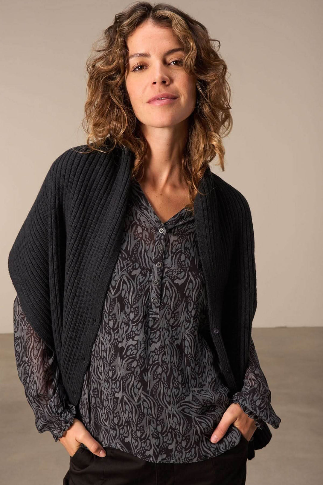 Foulard cape en tricot noir porté avec un haut à motifs, offrant élégance et confort.