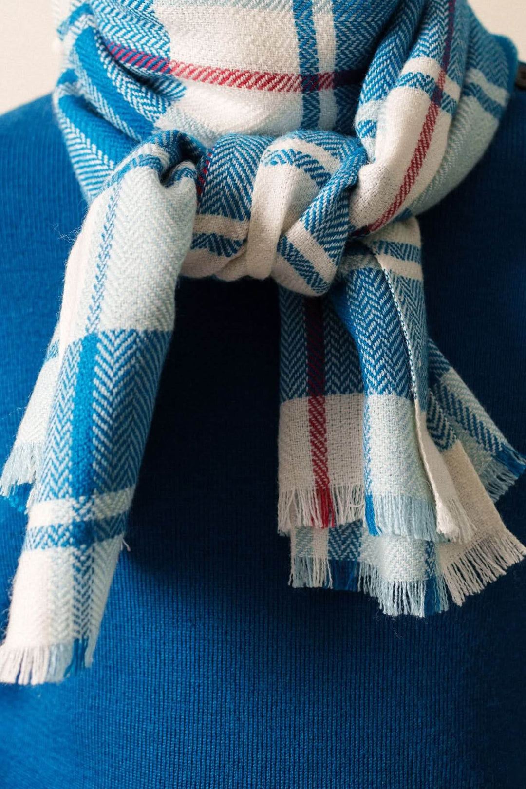 Foulard à carreaux doux et enveloppant bleu et rouge avec finition frangée, idéal pour tenues automnales et hivernales.