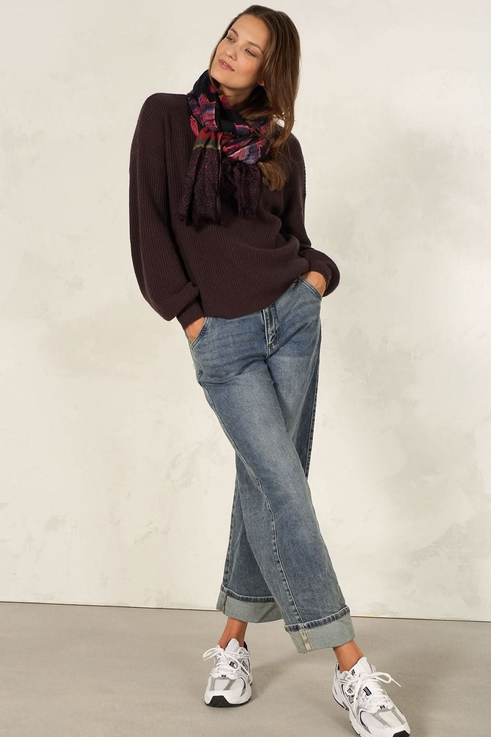 Femme portant un foulard décoratif, pull confortable et jeans, style élégant avec des baskets blanches.