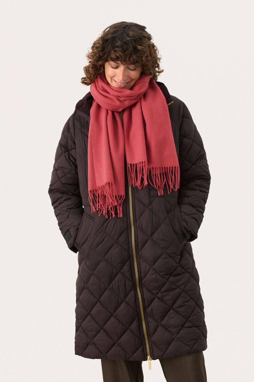 Femme portant une doudoune noire et un foulard en laine rose, souriante et élégante pour l'hiver.