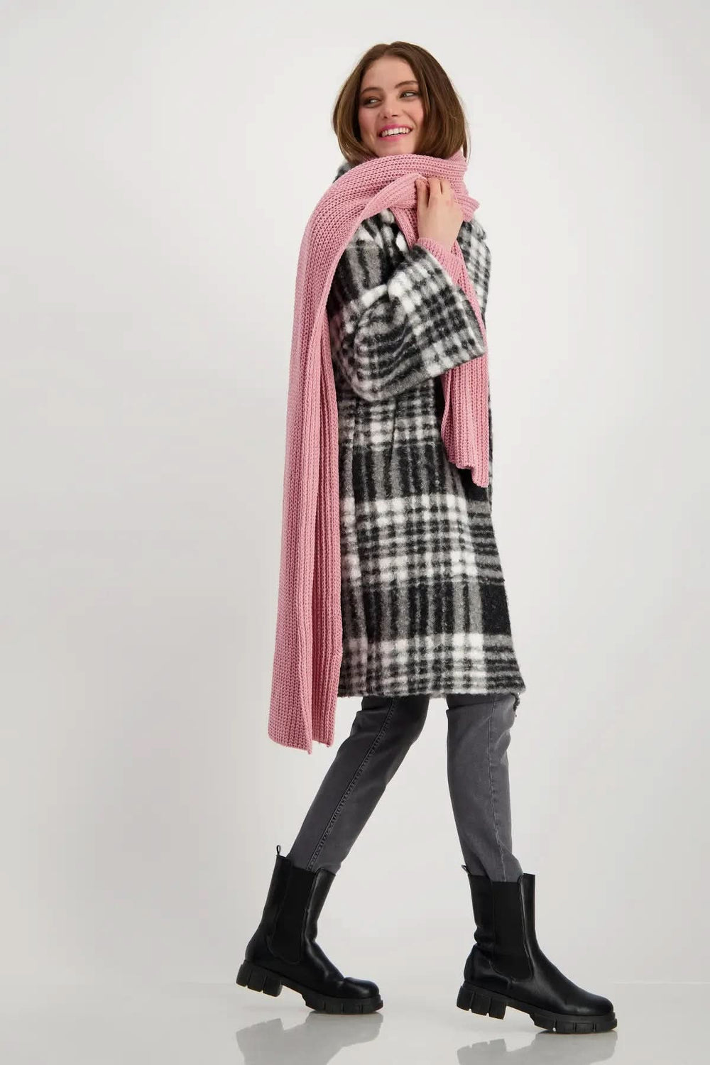 Femme souriante portant un foulard en tricot rose avec un manteau écossais, look moderne et élégant.