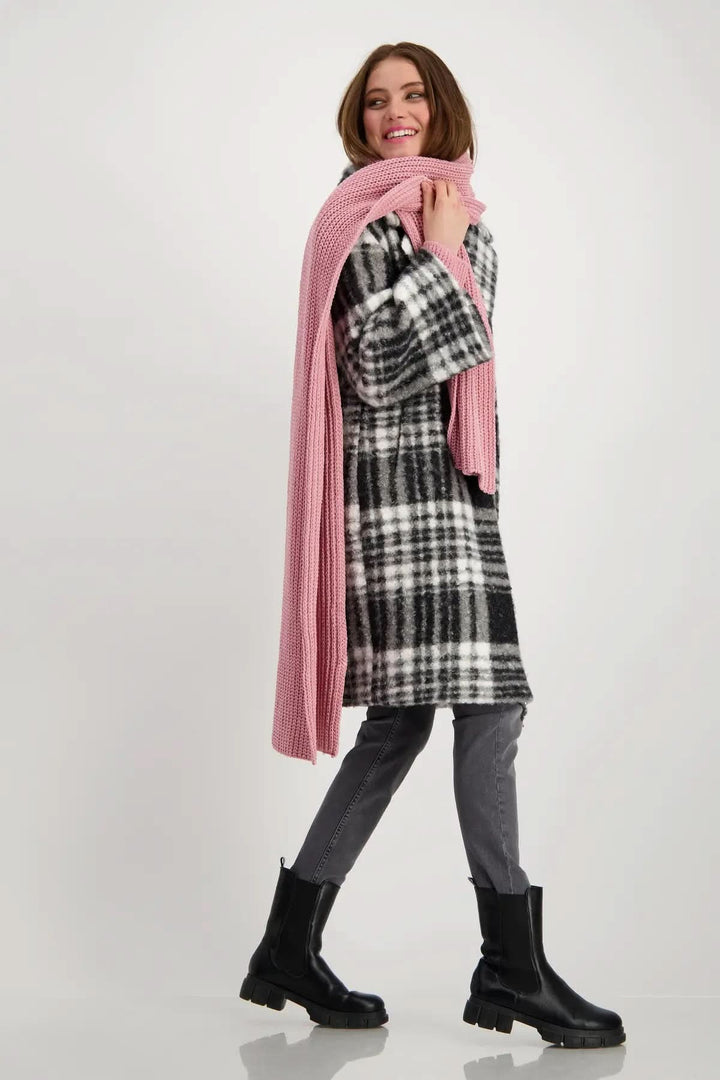 Femme souriante portant un foulard en tricot rose avec un manteau écossais, look moderne et élégant.