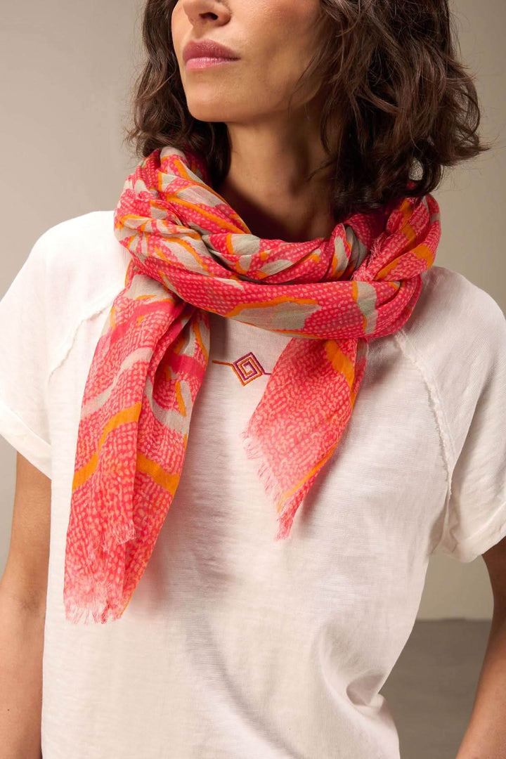 Foulard imprimé coloré drapé autour du cou, ajoutant une touche sophistiquée à une tenue décontractée.