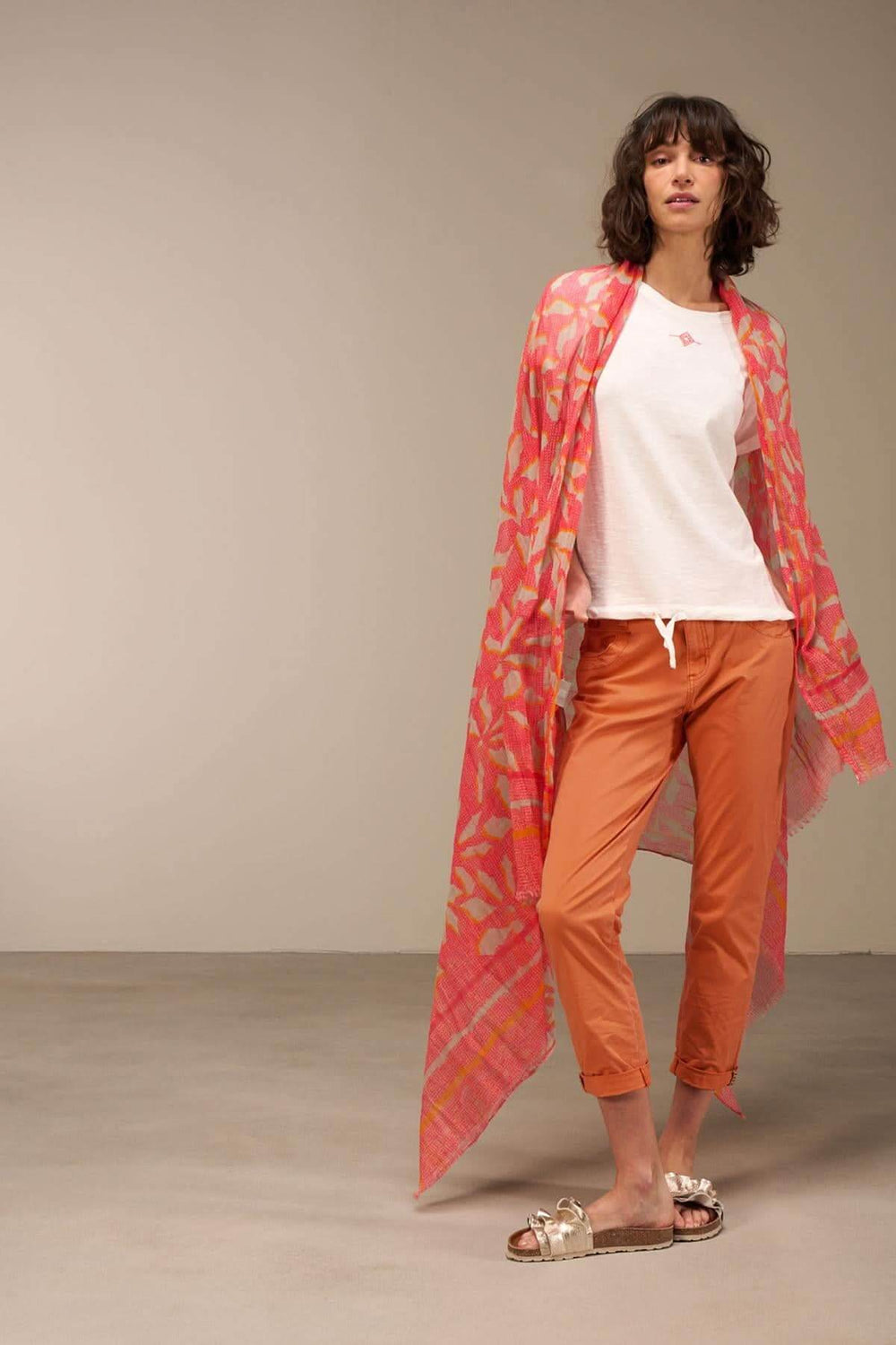 Foulard imprimé en coton bio, porté avec un haut blanc et un pantalon orange, ajoutant une touche sophistiquée.