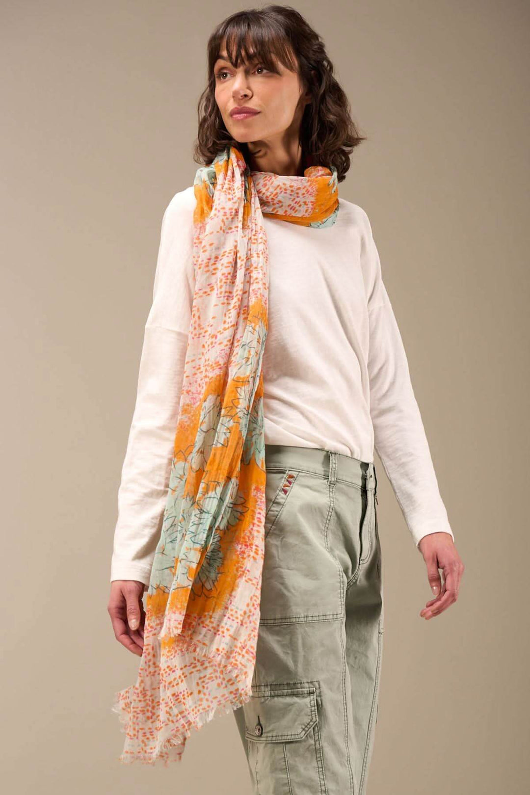 Foulard imprimé en coton bio, charme unique avec bords frangés, portée par un modèle dans une tenue décontractée.