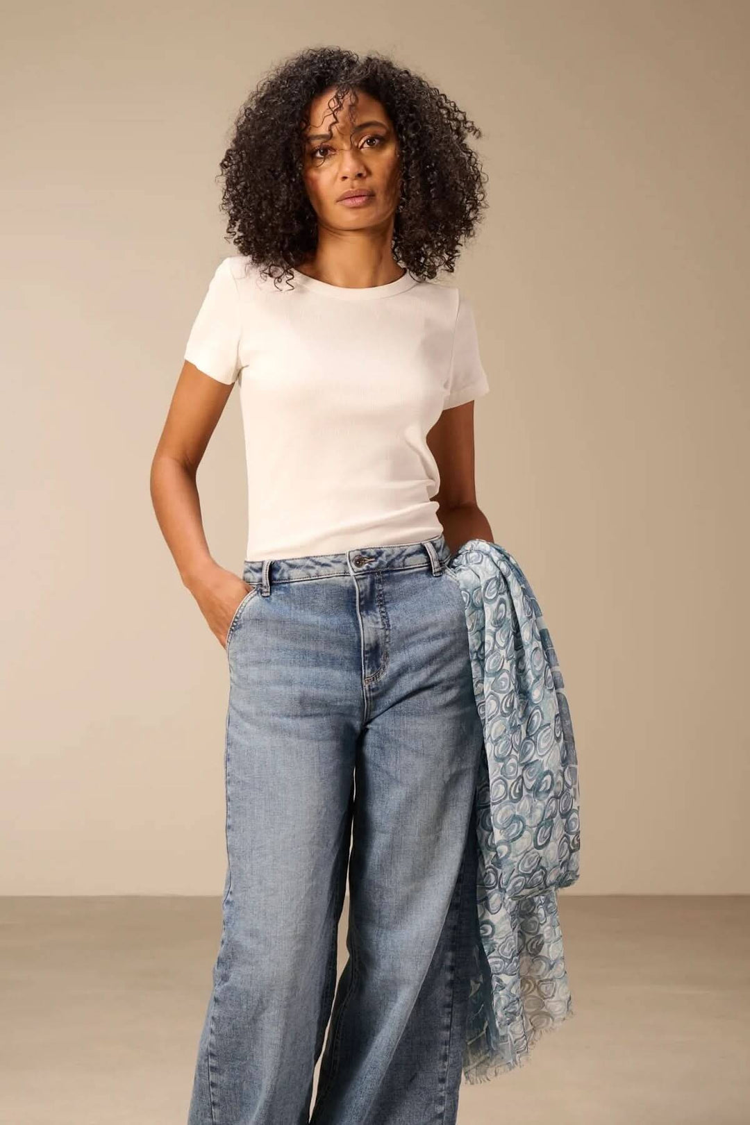 Femme portant une écharpe, foulard léger à imprimé bleu drapé, tenue décontractée avec un t-shirt blanc et un jean.