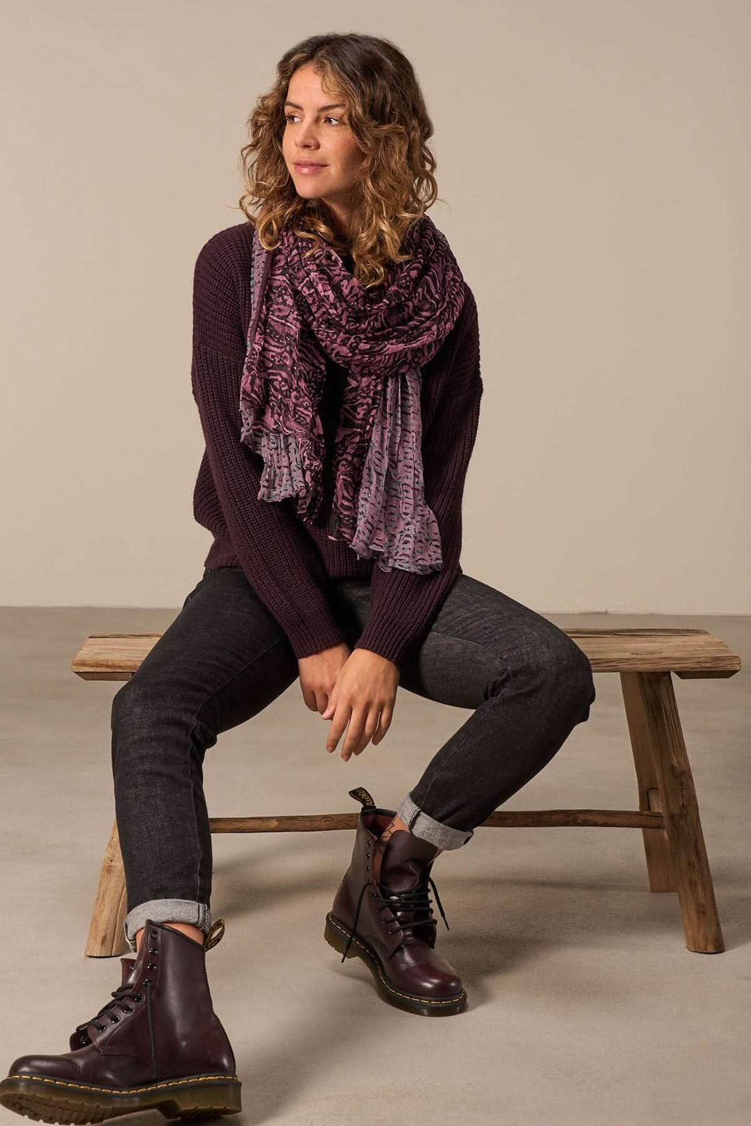 Femme portant un foulard à motif enroulé, associée à un pull et un jean, sur un banc en bois.