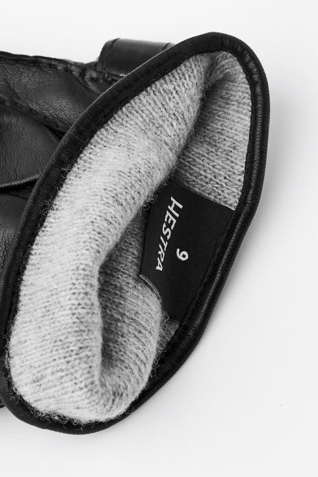 Intérieur d'une paire de gants en cuir noir avec doublure en laine grise, étiquette Hestra visible.