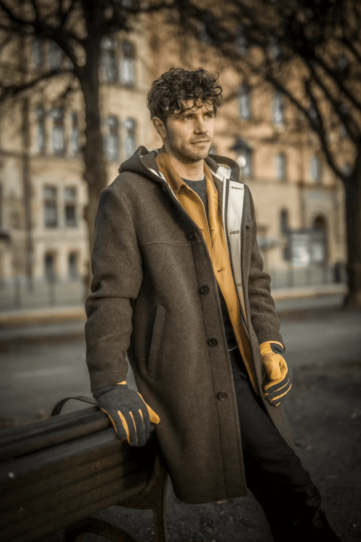 Homme dans un manteau en laine, portant des gants de cuir Noah, en arrière-plan urbain.