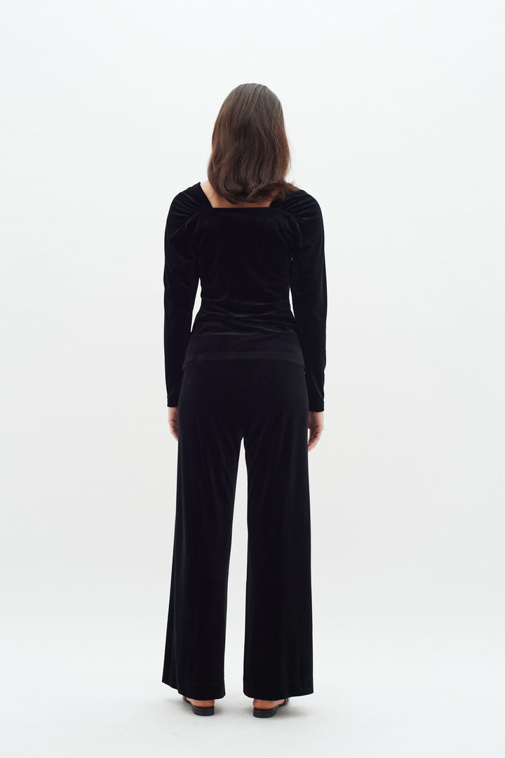 Femme vue de dos portant un haut en velours noir à col carré et pantalon assorti, style élégant et confortable.