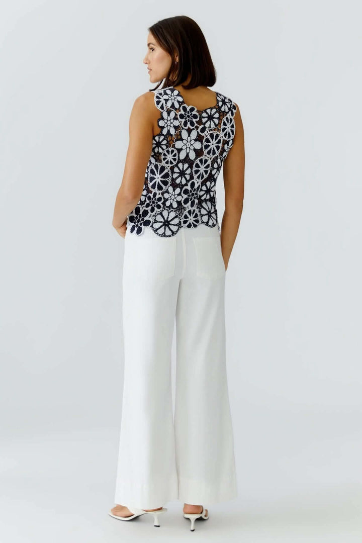Femme portant un haut coupe moderne minimaliste noir avec dos en dentelle florale, associé à un pantalon blanc fluide pour une allure élégante.