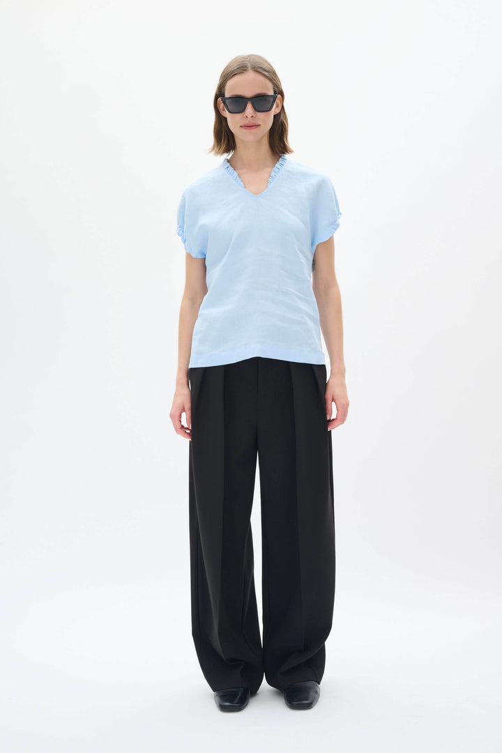 Haut en lin Rigitta en bleu clair avec encolure en V, manches courtes et pantalon noir élégant.