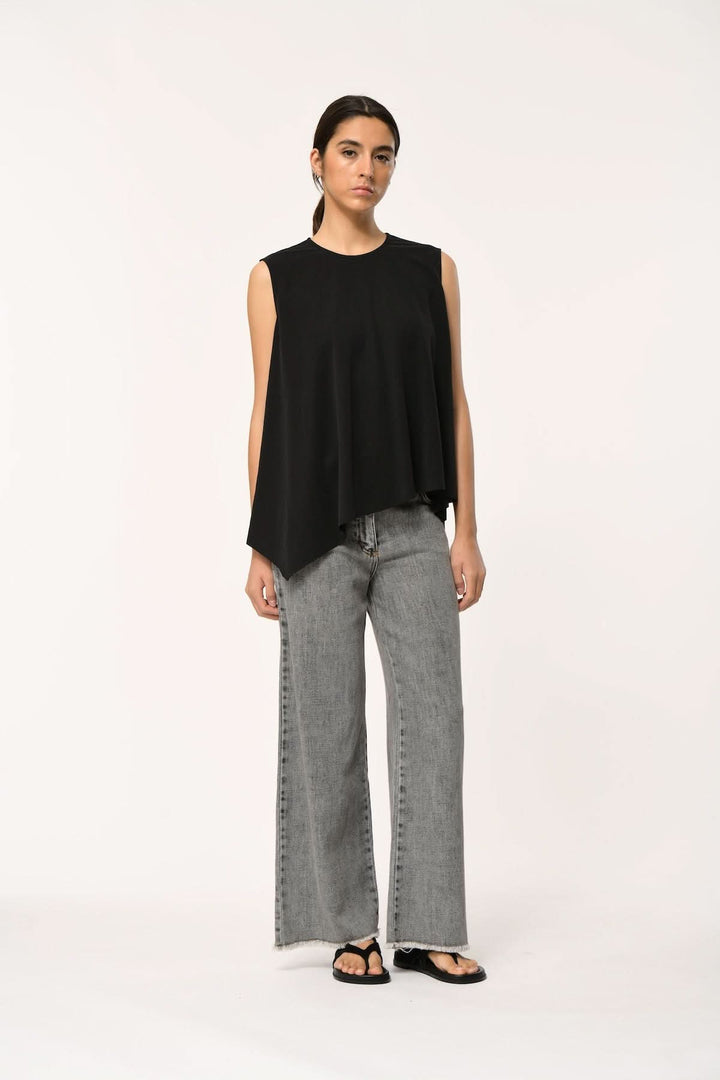 Modèle portant un haut fluide LORO asymétrique sans manches noir avec jean gris moderne.