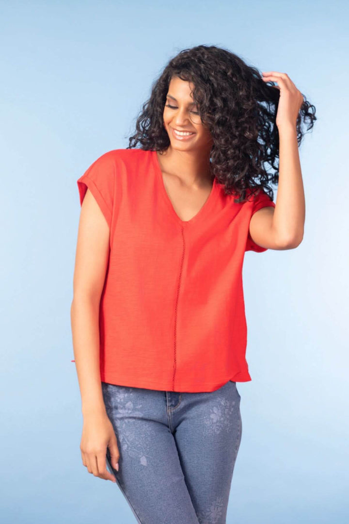 Femme portant un haut fluide col en V rouge, manches courtes, coupe décontractée, idéal pour une garde-robe moderne et polyvalente.